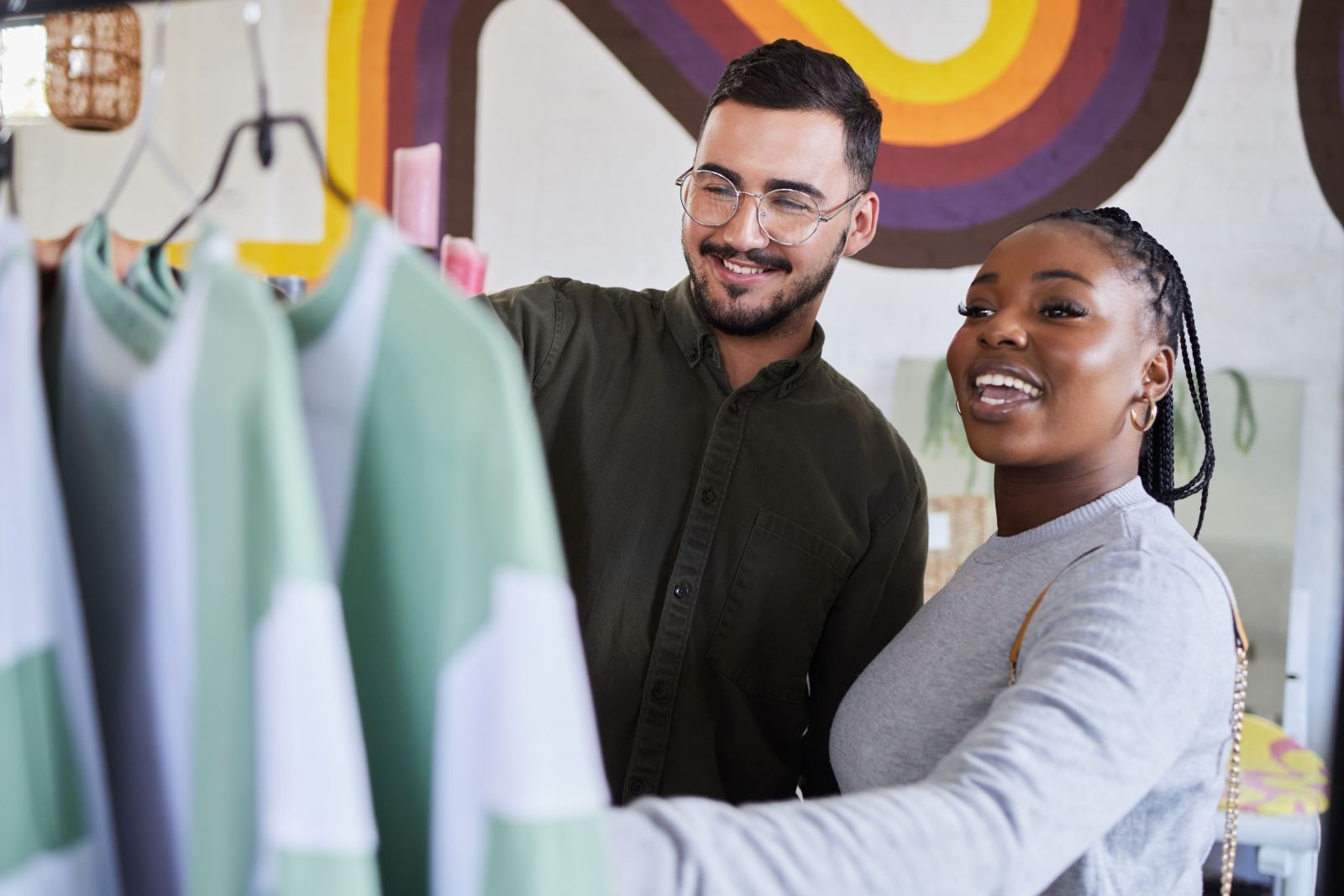 Two people happily browsing through clothes in a retail store, discussing and selecting items together.